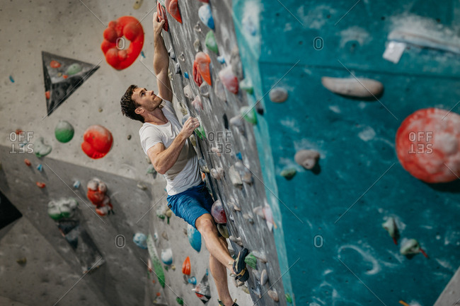 Male climber climbing up an artificial climbing wall in an indoor bouldering gym. Man making his way up a bouldering wall.