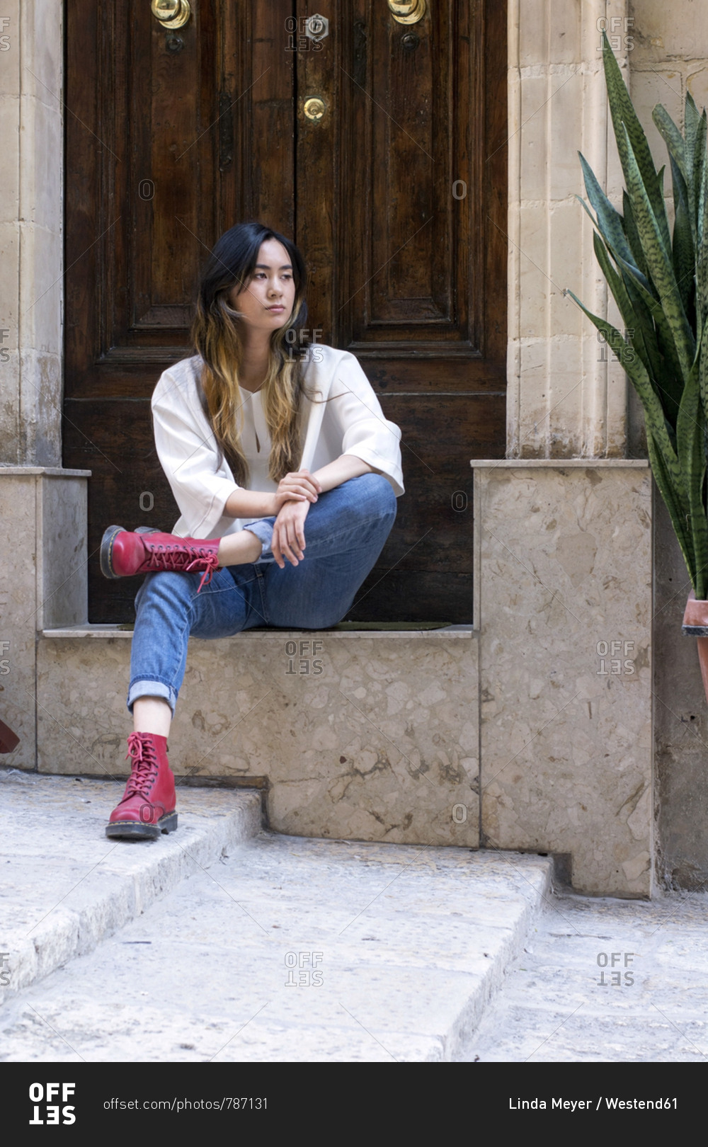 Portrait of young woman wearing red boots sitting on step in front of entry door