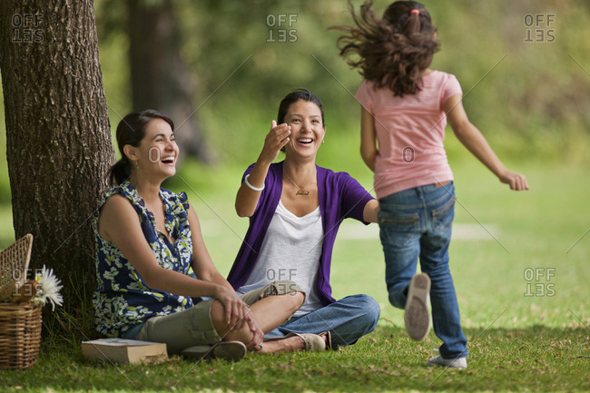 Young girl running towards her mother and a friend at the park.