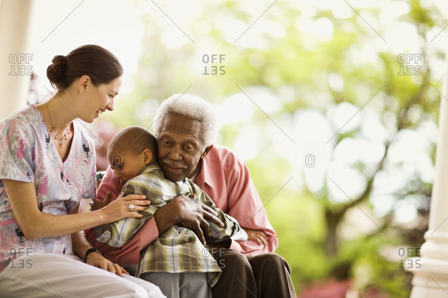 Nurse looks on happily as a senior man hugs a boy and she puts a supportive hand on the boy's arm.