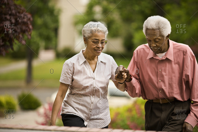 Senior couple hold hands as they walk up steps in a garden.