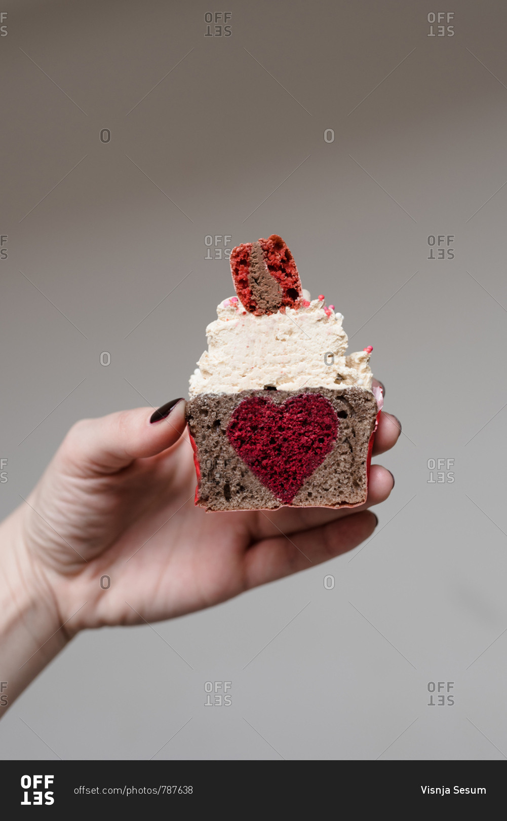 Woman holding a Valentine's day themed cupcake cut in half with heart shaped filling in the middle