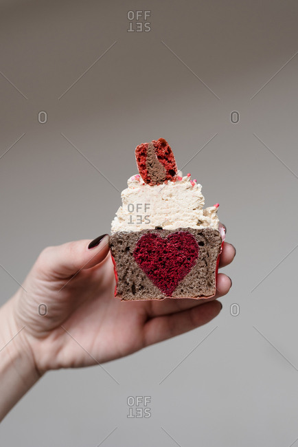 Woman holding a Valentine's day themed cupcake cut in half with heart shaped filling in the middle