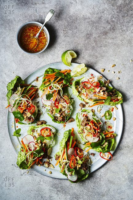 Six Vietnamese lettuce wraps shot from above with a wedge of lime and sauce at the top of the image. Ingredients include beef, rice noodles, carrot, cucumber, spring onions, chili, peanuts, coriander, mint and squeeze of lime.