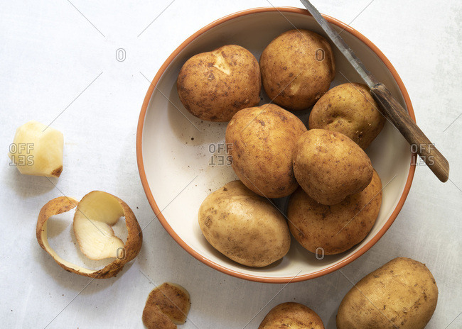 Brushed potatoes in a bowl with one peeled potato.