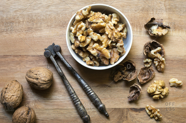 Cracked walnut pieces in a bowl beside whole walnuts and a vintage nut cracker.