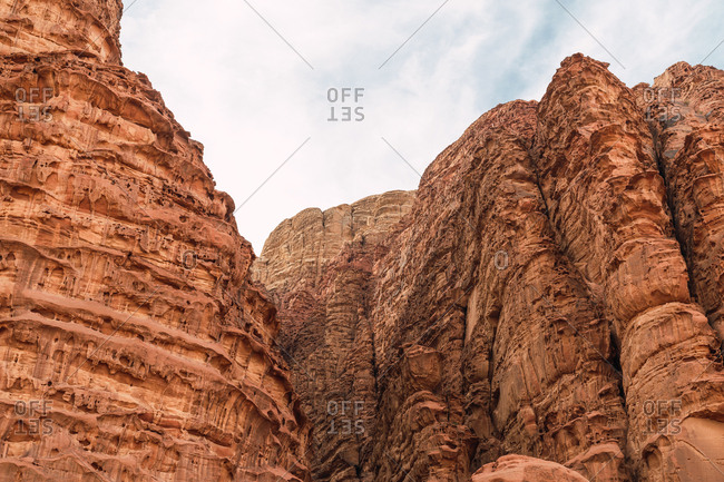 From below of high sandstone sheer cliffs with textured rough surface in desert of Wadi Rum, Jordan