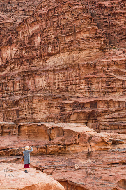 View at distance of traveling woman standing on sandstone rock against texture aged cliff in desert of Wadi Rum, Jordan