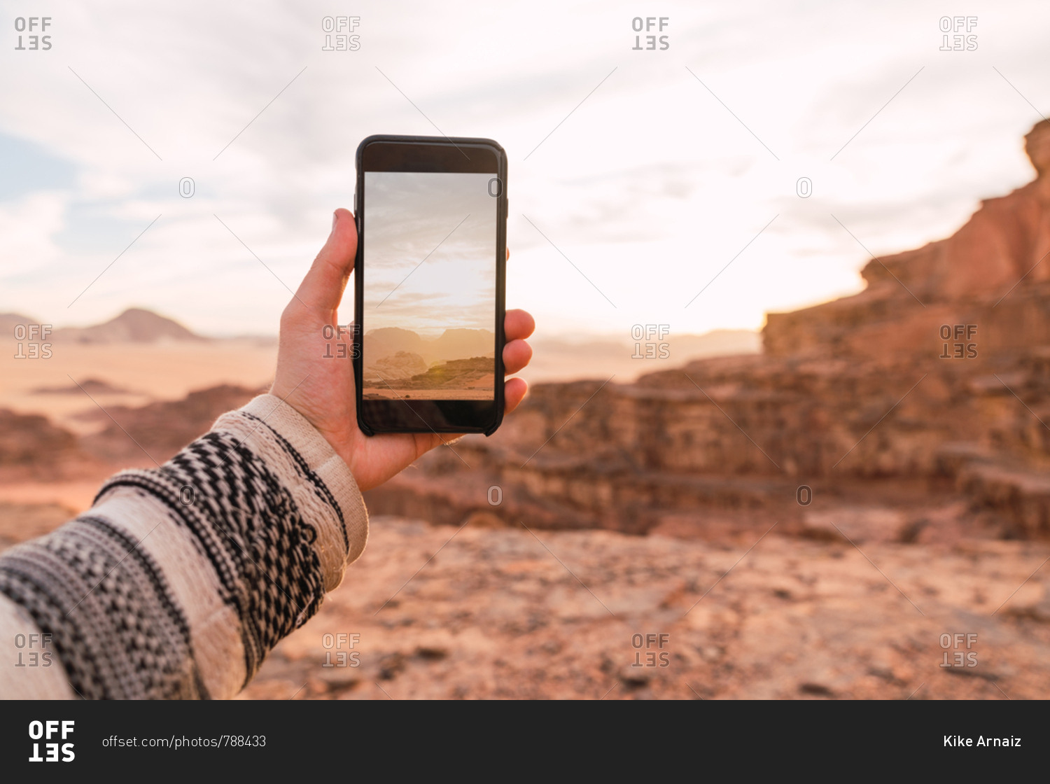 Crop male hand in sweater holding smartphone taking photo of picturesque desert of Wadi Rum desert in Jordan