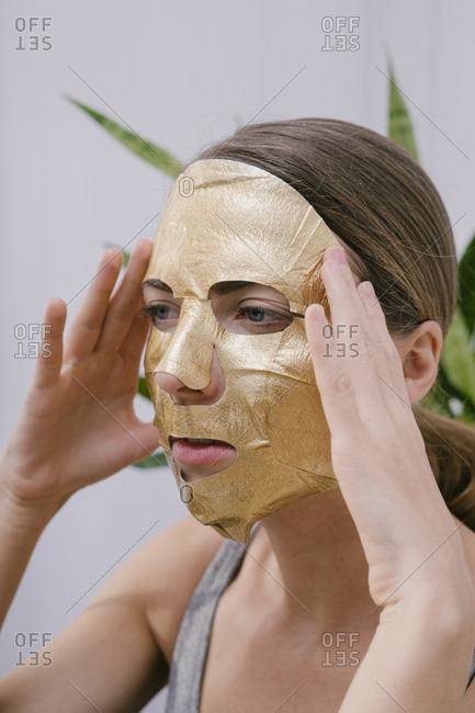 Young beautiful woman at home put on a golden face mask