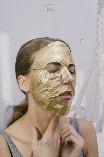 Young beautiful woman at home put on a golden face mask