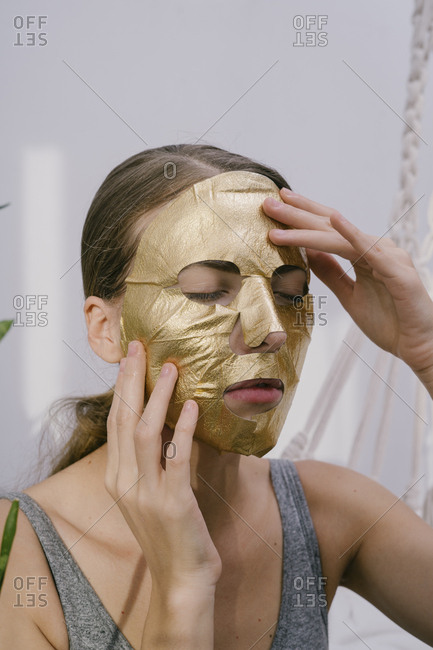 Young beautiful woman at home put on a golden face mask