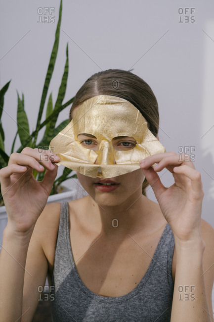 Young beautiful woman at home put on a golden face mask