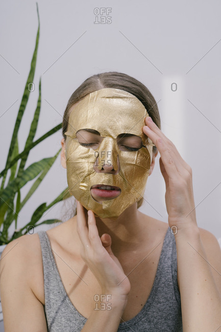 Young beautiful woman at home put on a golden face mask