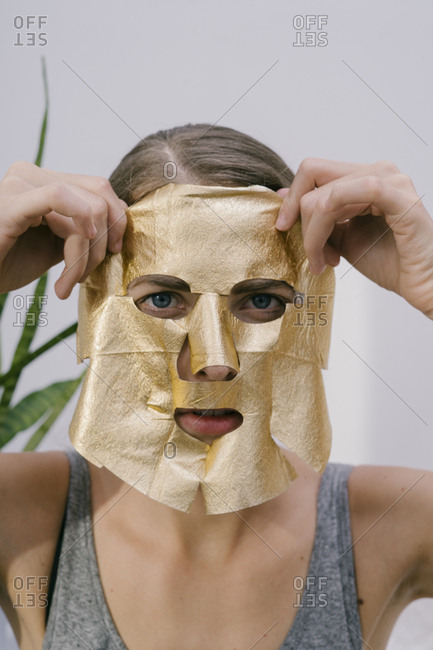 Young beautiful woman at home put on a golden face mask
