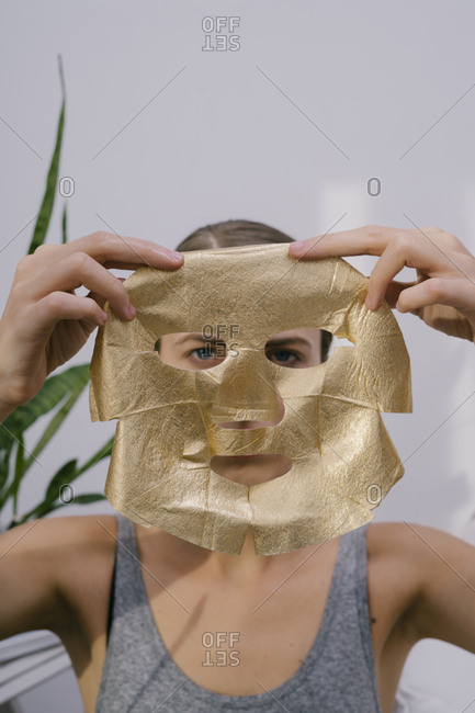 Young beautiful woman at home put on a golden face mask