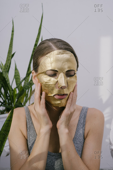 Young beautiful woman at home put on a golden face mask