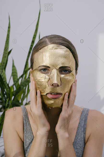 Young beautiful woman at home put on a golden face mask