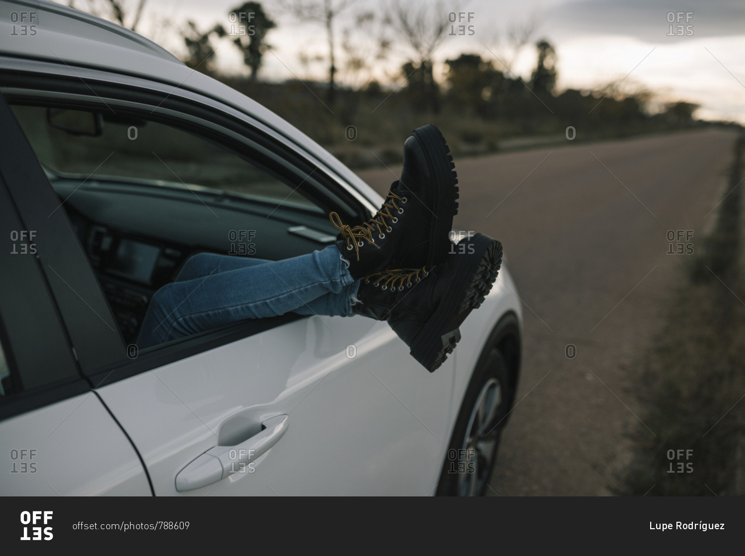 Legs of a woman with boots coming out the window of a car at sunset
