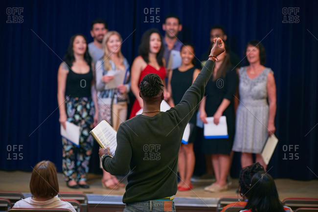 Male conductor with arm raised directing choir in auditorium