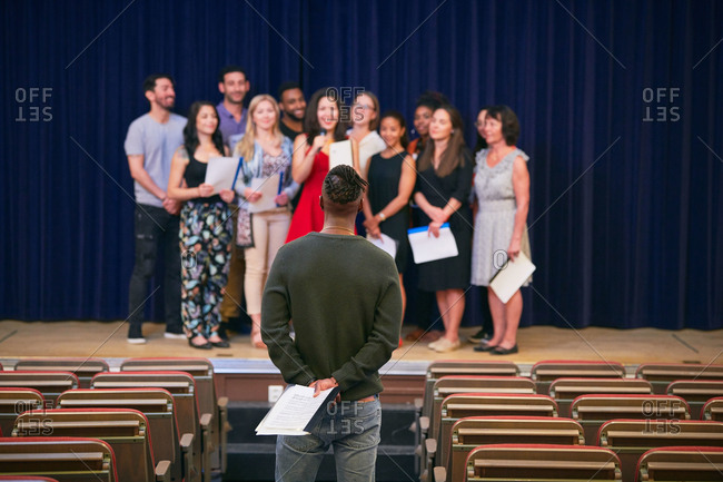 Musical teacher listening to choir on stage in auditorium of language school