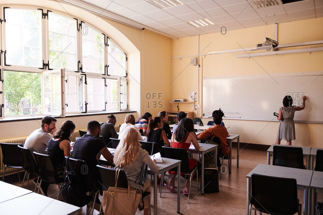 Teacher writing on whiteboard while students sitting in classroom