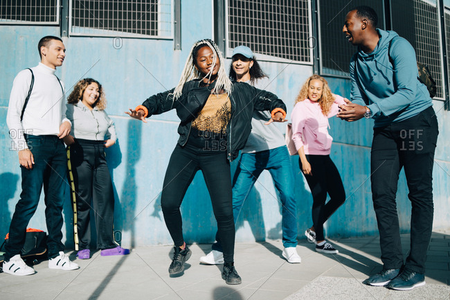 Smiling friends looking at teenage girl dancing on sidewalk in city