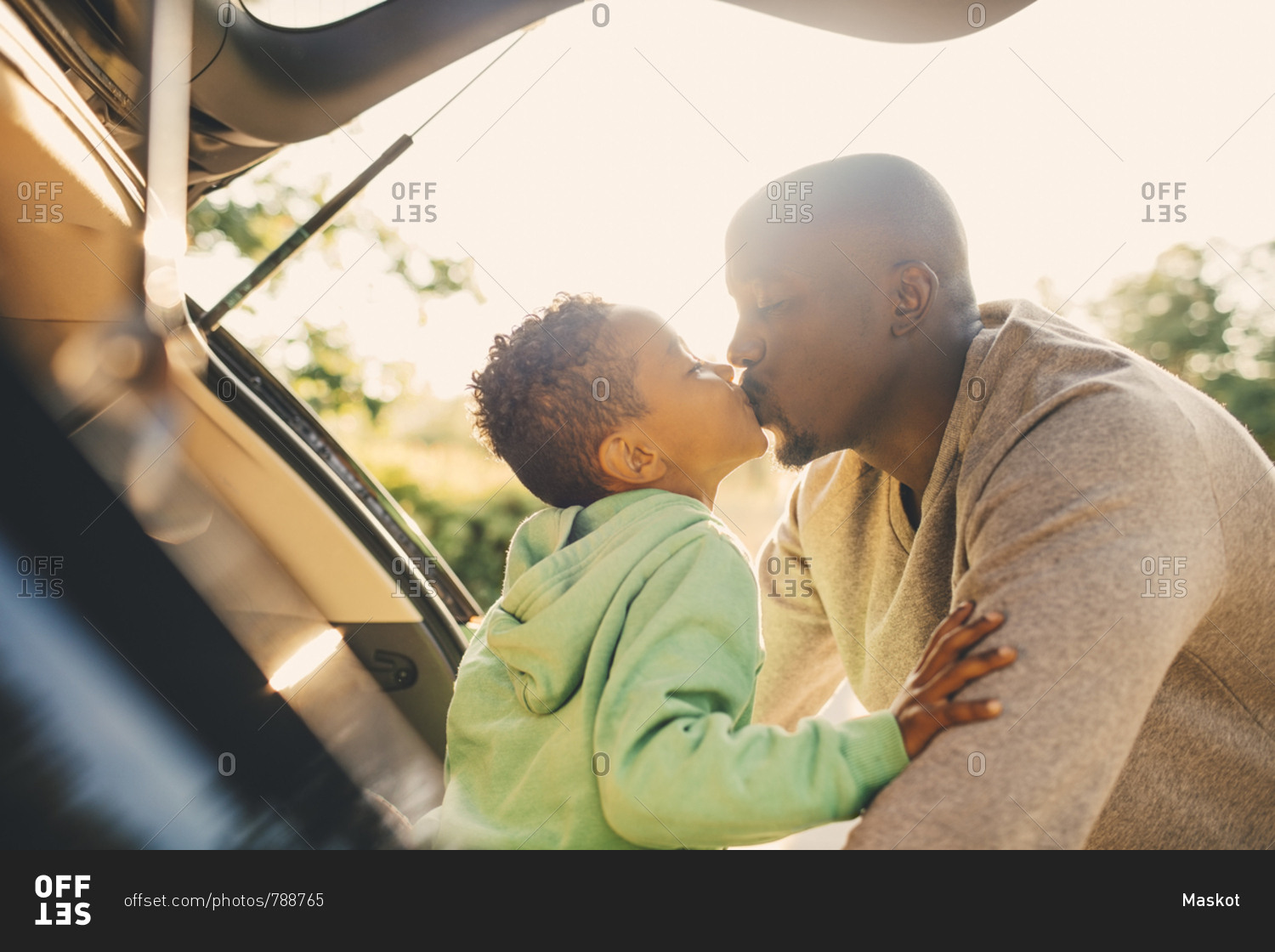 Father kissing son sitting in car trunk