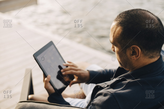 High angle view of man using digital tablet at patio by lake