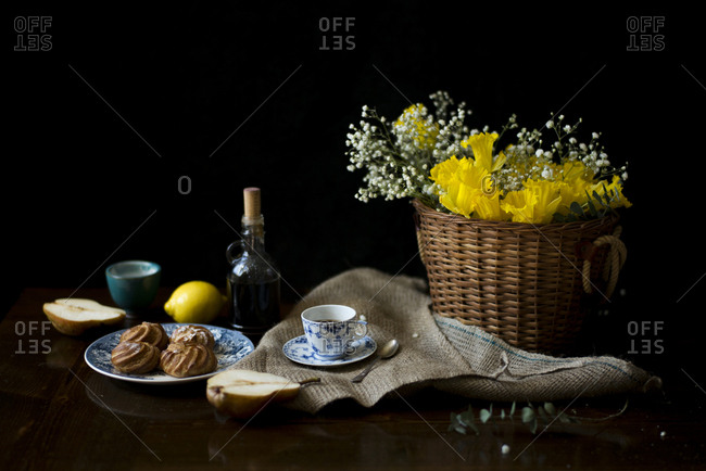 Yellow daffodils in a woven basket with coffee and dessert on a table