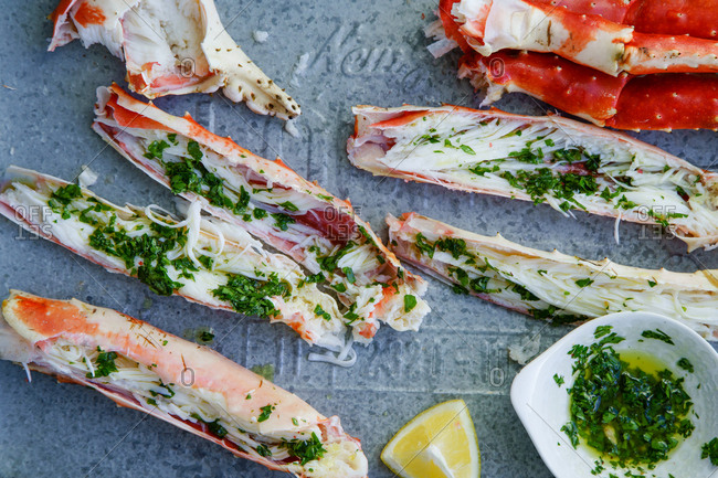 Cooked and cut king crab legs with parsley butter served on metallic tray