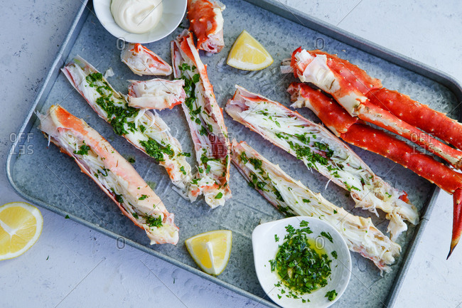 Cooked and cut king crab legs with parsley butter served on metallic tray