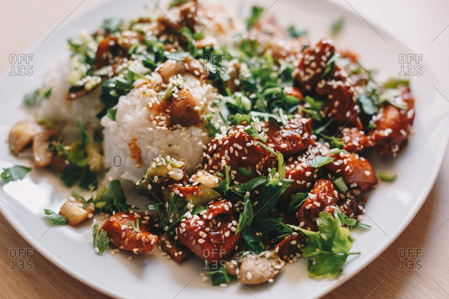 Top view closeup shot of teriyaki chicken with cooked rice, served on a white plate against an isolated wooden table background. Horizontal image.