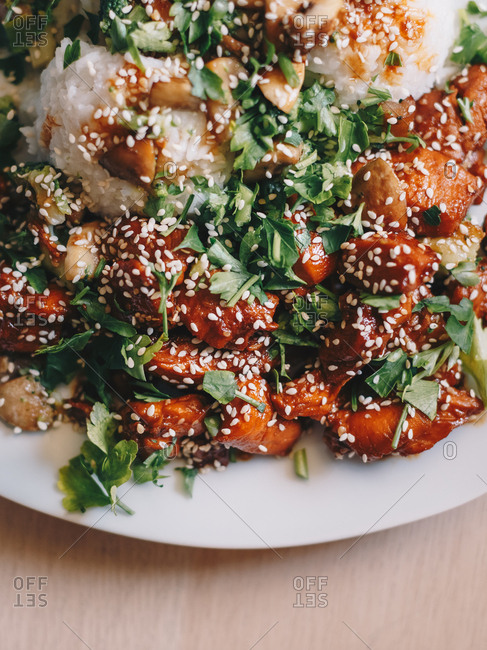 Top view close-up shot of teriyaki chicken with cooked rice, served on a white plate against an isolated wooden table background. Vertical image.