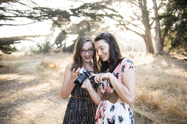 Happy sisters looking photographs in camera while standing against trees at forest