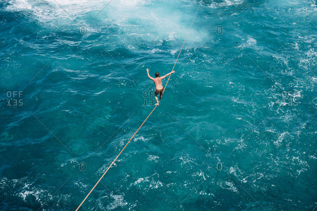 High angle view of carefree young man practicing slacklining over sea