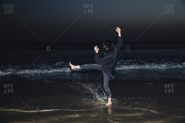 Side view of playful woman playing with water at beach against sky