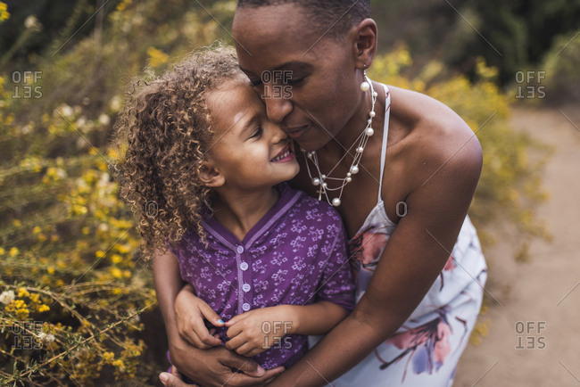 Mother embracing smiling daughter while standing against plants in park