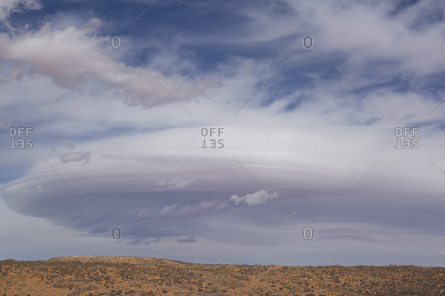 Scenic view of arid landscape against cloudy sky during sunny day