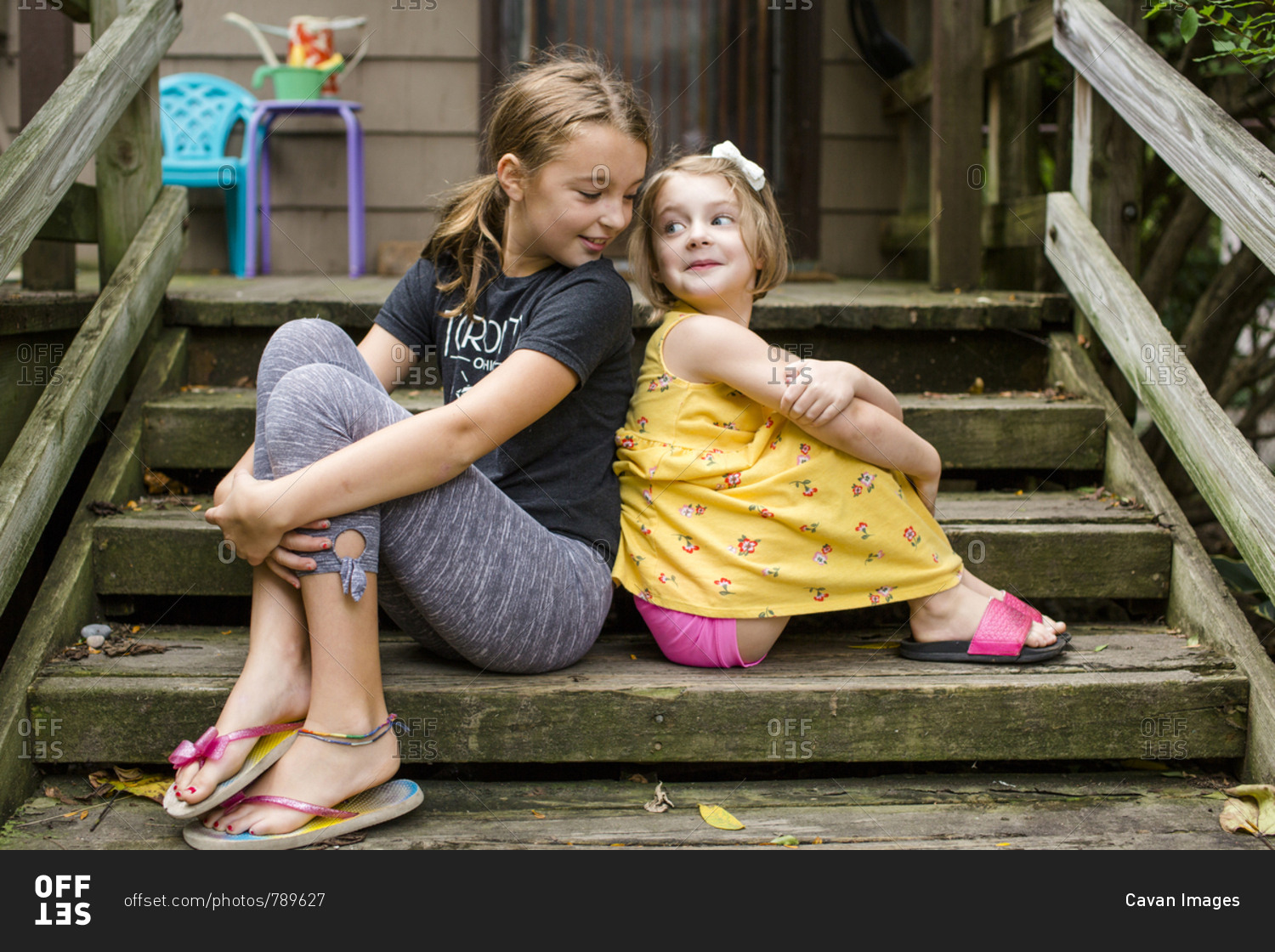 Cute sisters looking at each other while sitting on steps against house in yard