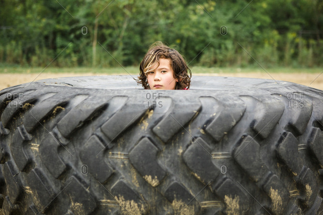 Portrait of cute boy peeking through dirty tire against plants
