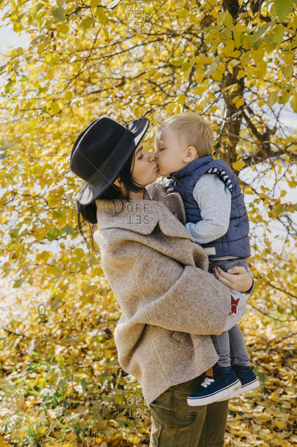 Side view of mother kissing son while standing against trees in park during autumn