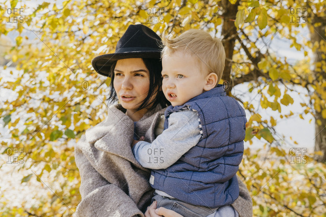 Mother carrying cute son while standing against trees at park during autumn