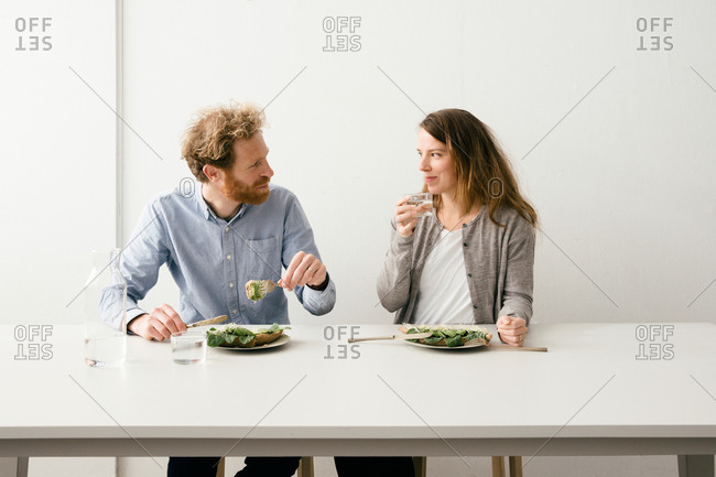 Thirty something European couple sitting down for a avocado sandwich lunch together looking at each other.