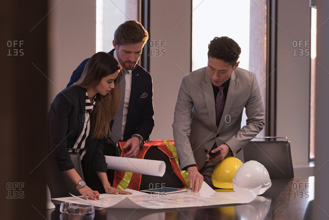 Side view of business people discussing over blueprint in the conference room surrounded of safety objects at workplace
