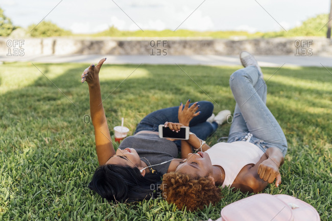 Two happy female friends relaxing in a park listening to music