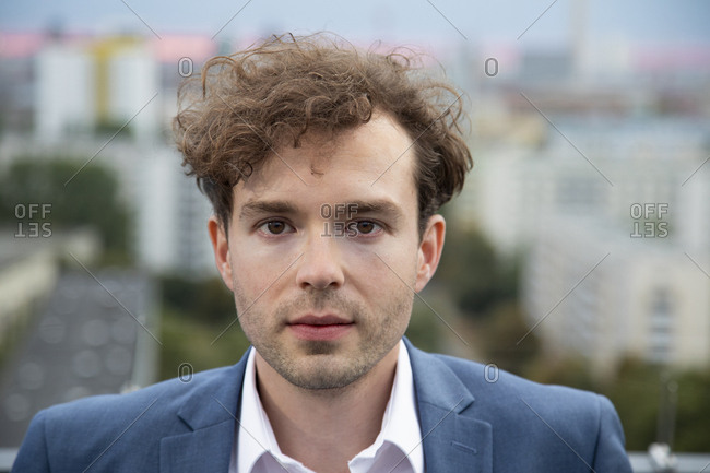 Portrait of businessman with stubble and curly brown hair on roof terrace in the evening