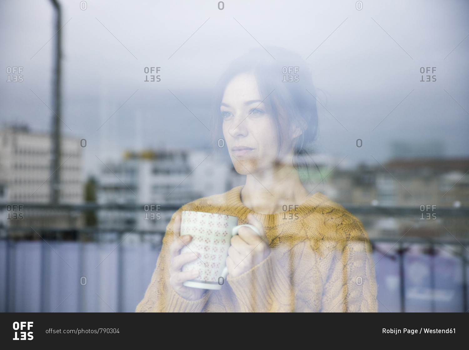 Sad woman standing at the window- drinking tea