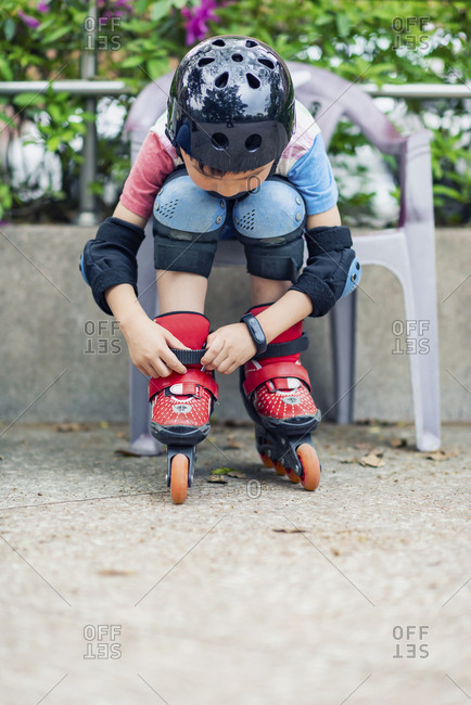 Little kid sit on chair and put on line skates, close up