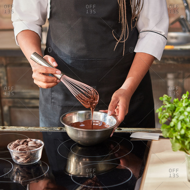 Professional confectioner's mix and warm melted chocolate on a hob for preparation homemade sweets at the kitchen table. Step by step process of chocolate preparing